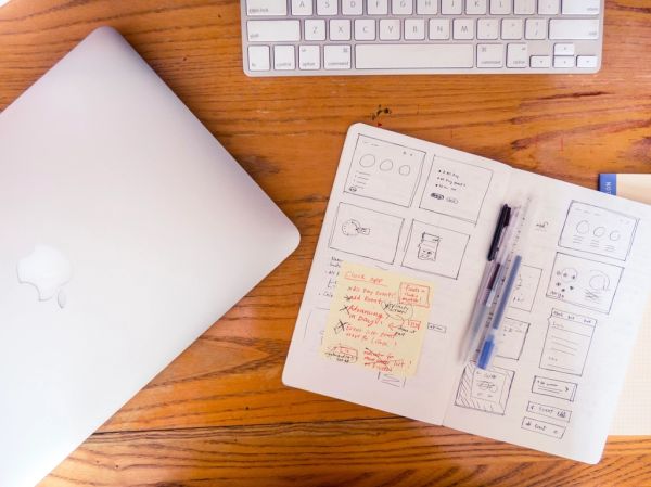 Schetsboek met wireframes voor een nieuw websiteontwerp naast een laptop