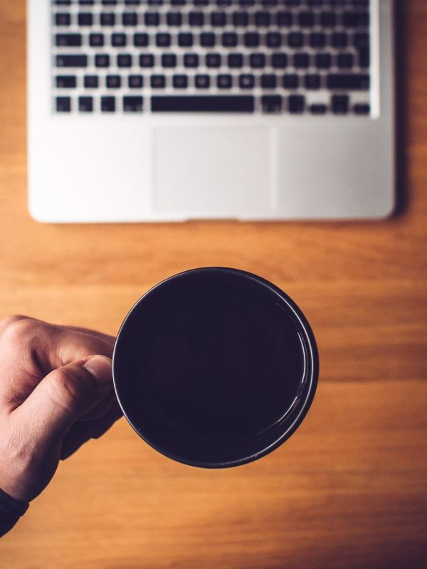Hand met kop koffie boven een laptop, symbool voor een koffieabonnement
