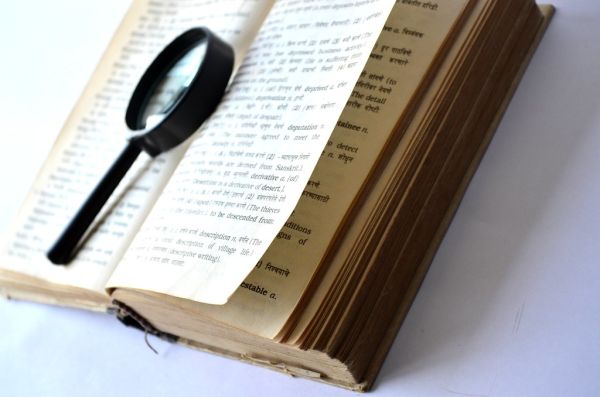 Vergrootglas op een openliggend woordenboek als symbool voor zoeken